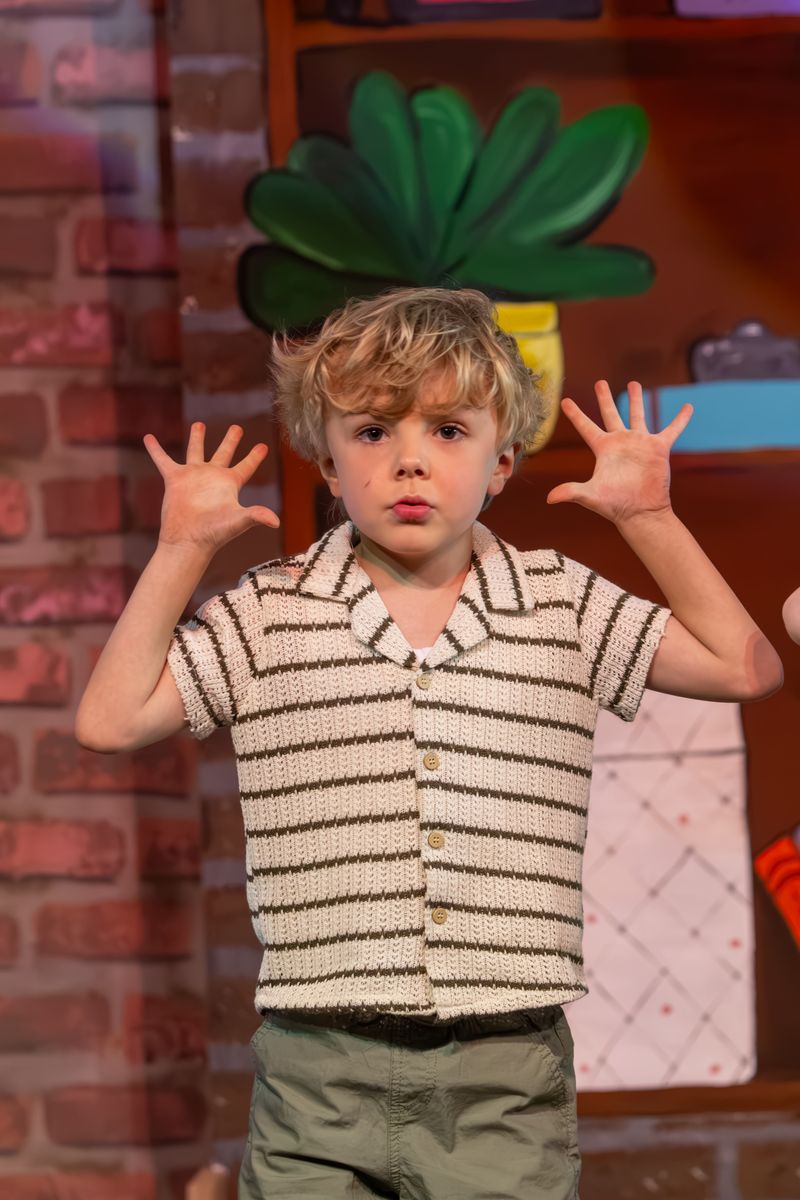 A curly-haired boy in a striped knit shirt with both hands raised mid-song